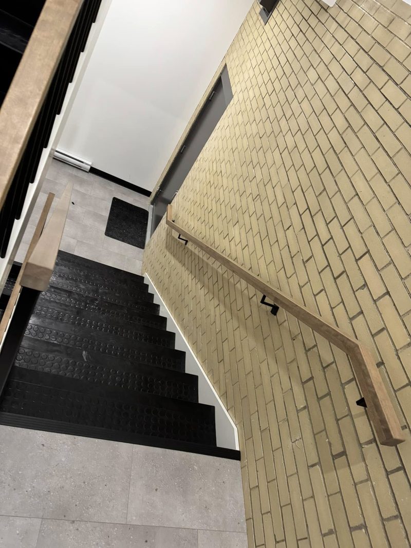 Escalier commercial à marches noires et main courante de bois le long d'un mur de brique