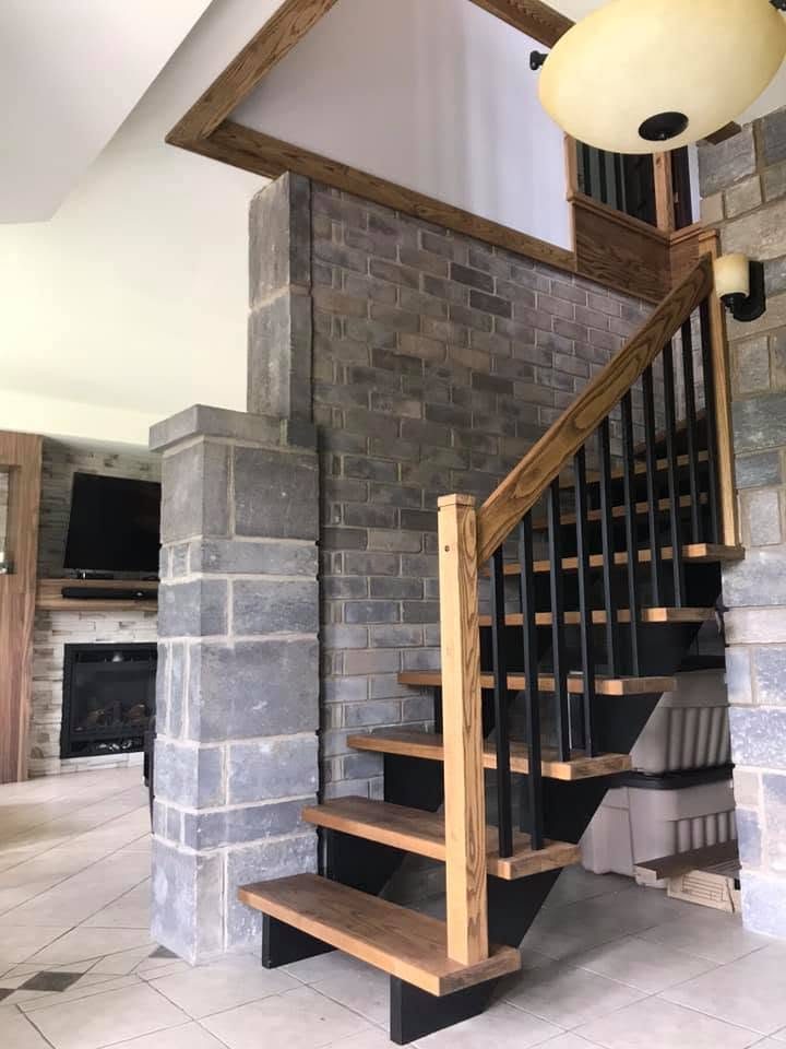 Escalier flottant en bois et barreaux noirs à côté d'un foyer de pierre