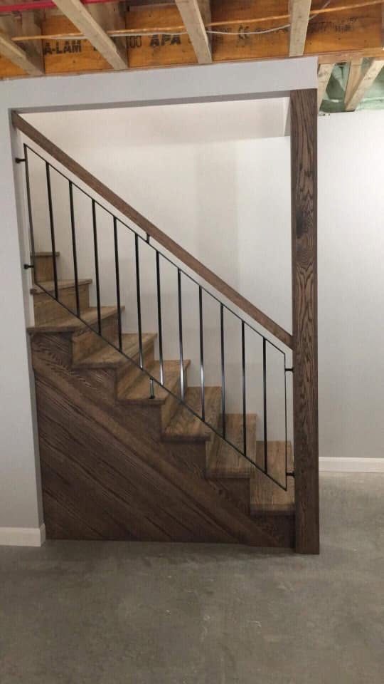 Escalier en bois foncé avec barreaux noirs dans une cage encadrée de bois